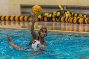 Water polo player in action, preparing to throw the ball while another player attempts to defend in the pool.