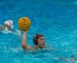 A female water polo player prepares to throw the ball while teammates swim in a blue pool.