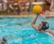 A young female water polo player prepares to throw a ball during a game in a competitive swimming pool.