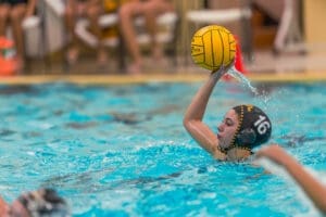 A young female water polo player prepares to throw a ball during a game in a competitive swimming pool.