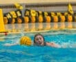 Water polo athlete focuses on the game while swimming, with a yellow ball in play and an intense competitive atmosphere.