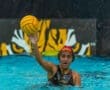 Young female water polo player shooting a ball in an underwater arena, showcasing athleticism and team spirit.