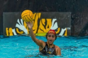 Young female water polo player shooting a ball in an underwater arena, showcasing athleticism and team spirit.
