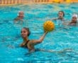 Water polo athlete poised to pass the ball during a match, surrounded by teammates in a vibrant pool setting.