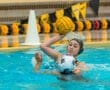 Water polo action shot: a player prepares to pass the ball while defending against an opponent in a pool.