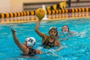 A water polo player prepares to throw the ball during a match in a swimming pool, showcasing athletic skill and strategy.