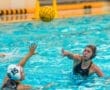 Water polo players compete in a fast-paced game, one athlete passing the ball while another reaches to defend.