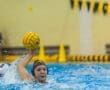 Young female water polo player in action, throwing a ball amidst splashes in a competitive pool environment.