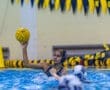 Player poised to throw a water polo ball during a match in a competitive swimming pool setting.
