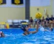 Girl in a water polo match, about to pass a ball, with water splashing around her in a competitive atmosphere.