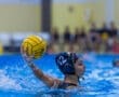 Female water polo player prepares to throw a yellow ball in a pool, showcasing athleticism amidst splashing water.