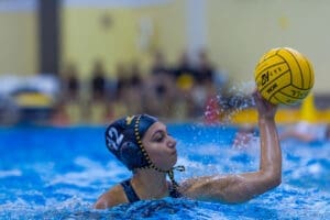 A water polo player in action, poised to throw the ball during a competitive match in an aquatic setting.