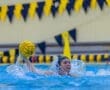 Water polo player throwing the ball during a game, with water splashing around and team colors in the background.