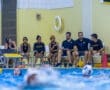 Water polo team during a match, with players and coaches on the sidelines, observing the action in the pool.