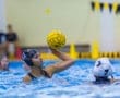 Youth water polo player in action, preparing to throw a yellow ball during a competitive match in a swimming pool.