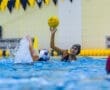 Water polo action shot: a player prepares to throw a yellow ball while splashing water, showcasing athleticism and teamwork.