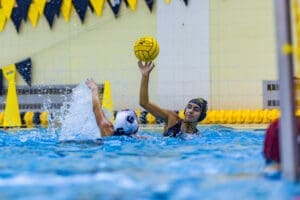 Water polo action shot: a player prepares to throw a yellow ball while splashing water, showcasing athleticism and teamwork.