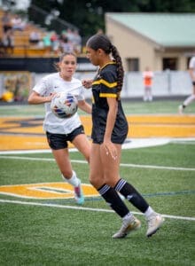 Two female soccer players compete for the ball on a field, showcasing athleticism during a match.