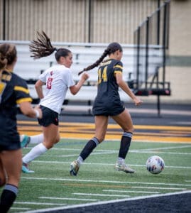Two female soccer players compete for the ball on a vibrant field during an intense match.