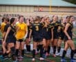 Girls' soccer team celebrating a goal, showcasing teamwork and excitement on the field during a match.