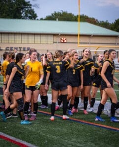 Girls' soccer team celebrating a goal, showcasing teamwork and excitement on the field during a match.