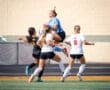 Goalkeeper jumps to catch the ball while teammates defend against opponents during an intense soccer match.