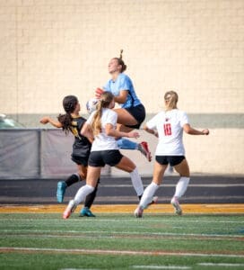 Goalkeeper jumps to catch the ball while teammates defend against opponents during an intense soccer match.