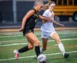 Two female soccer players compete for the ball on a vibrant turf field during an intense match.