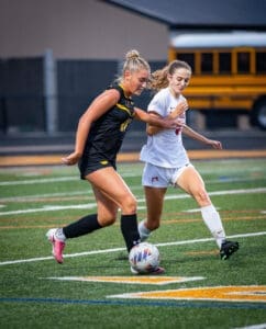 Two female soccer players compete for the ball on a vibrant turf field during an intense match.