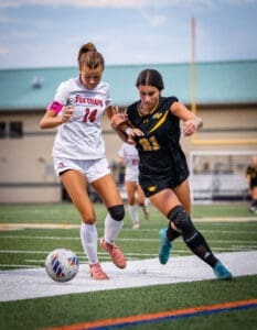 Two young female soccer players compete for the ball on a turf field, showcasing athleticism and teamwork in action.