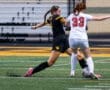 Two high school girls soccer players compete for the ball on a turf field during a match. Intense sports action captured.