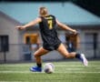 Female soccer player in action, wearing black jersey with Tigers and number 7, kicking a soccer ball on the field.