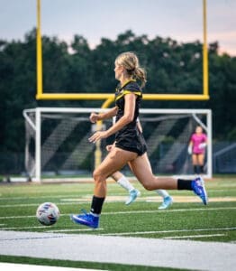A soccer player sprinting on the field, showcasing athleticism and determination during a match at dusk.