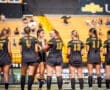 Female soccer players in black jerseys lined up on the field, smiling and interacting before a game.