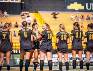 Female soccer players in black jerseys lined up on the field, smiling and interacting before a game.