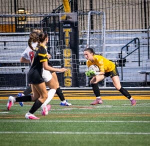 Goalkeeper in yellow makes a save during a soccer match, with players in action on the field.
