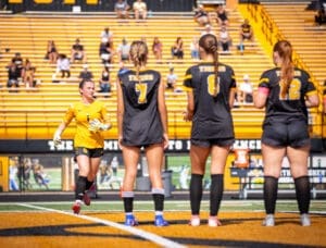Goalkeeper runs onto the field as her teammates prepare for a soccer match, showcasing team spirit and strategy.