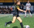 Young female soccer player in black uniform prepares to kick the ball on the field during an energetic game.