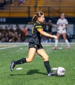 Young female soccer player in black uniform prepares to kick the ball on the field during an energetic game.