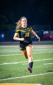 Soccer player in a black and yellow uniform, sprinting on a field during a night game.