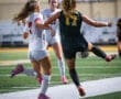 Two female soccer players compete for the ball on a well-lit field during a night match, showcasing athleticism and skill.