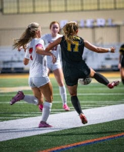 Two female soccer players compete for the ball on a well-lit field during a night match, showcasing athleticism and skill.