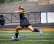 Girl in black soccer uniform kicking a ball on a field, showcasing athleticism and focus during a game.