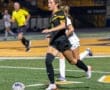 High school female soccer player in action, dribbling the ball during a night game on a turf field.