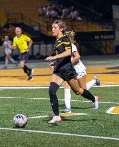 High school female soccer player in action, dribbling the ball during a night game on a turf field.
