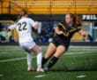 Two female soccer players compete for the ball on a green field, showcasing athleticism and sportsmanship during a match.