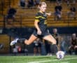 Youth soccer player kicking a ball on a field, showcasing athleticism under stadium lights during a match.