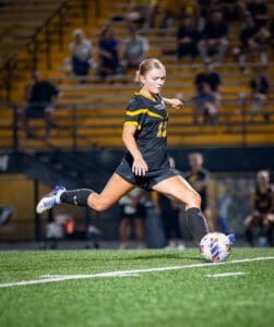 Youth soccer player kicking a ball on a field, showcasing athleticism under stadium lights during a match.