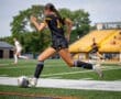 Soccer player in action, wearing black uniform, sprinting on the field with a ball during a game.