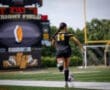 Female soccer player in black jersey dribbles ball on Wright Field, game scoreboard shows time remaining.